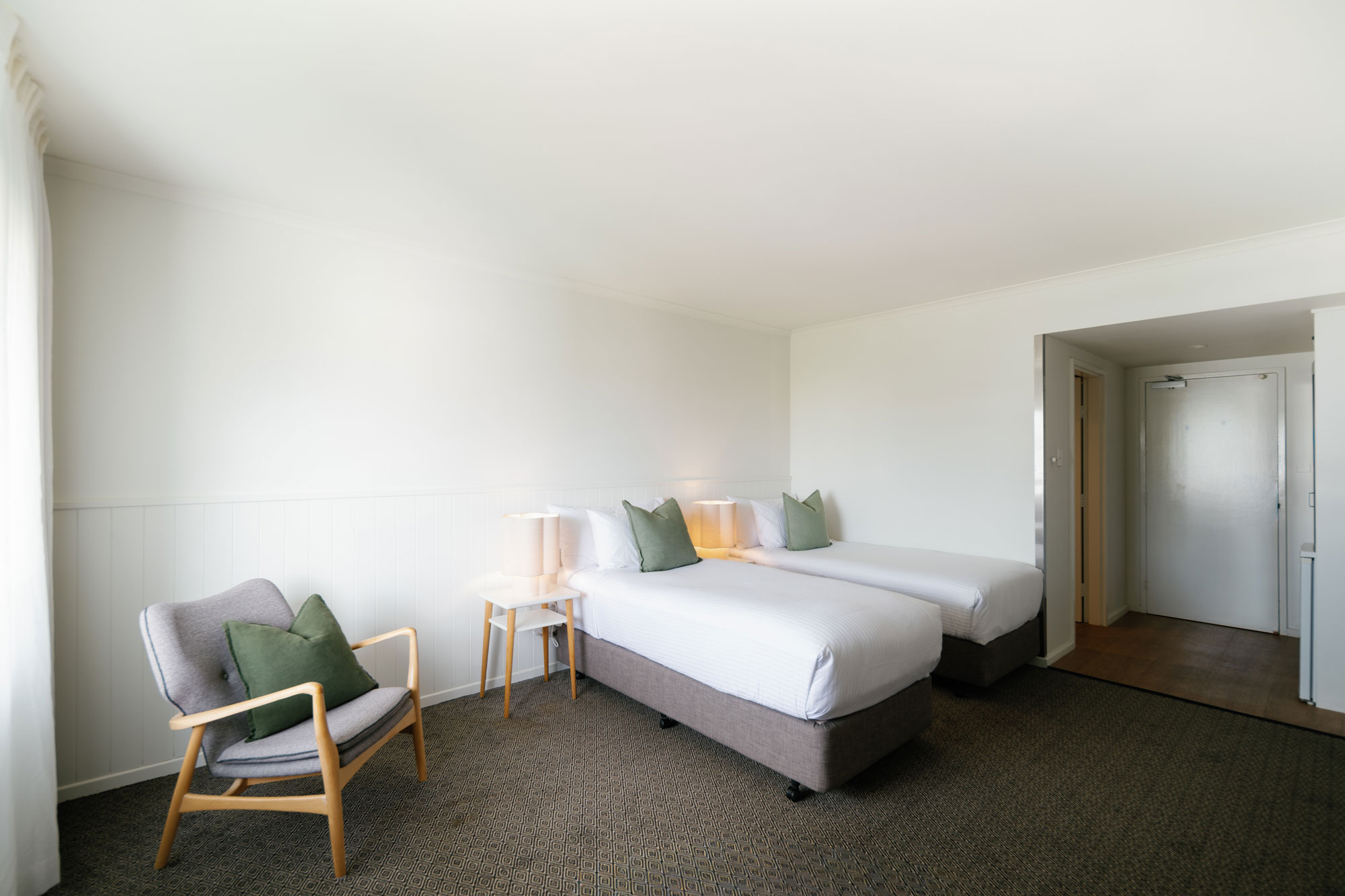 The Leea Darwin hotel room with two single beds and a grey armchair.